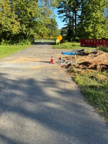 An asphalt driveway cut open and backfilled with compacted stone before patching.