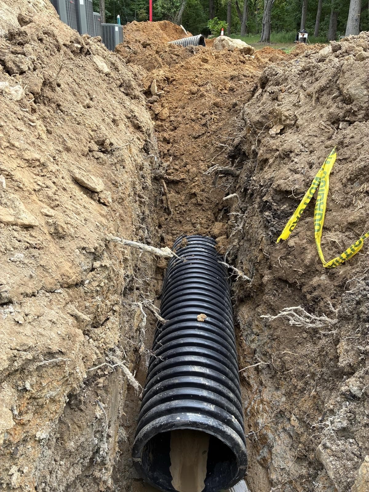 Large corrugated drainage pipe laid in a freshly dug trench beside a house.